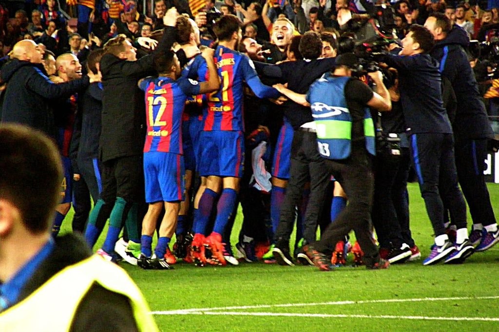 Barcelona players and staff piled together celebrating on the Camp Nou pitch at night.