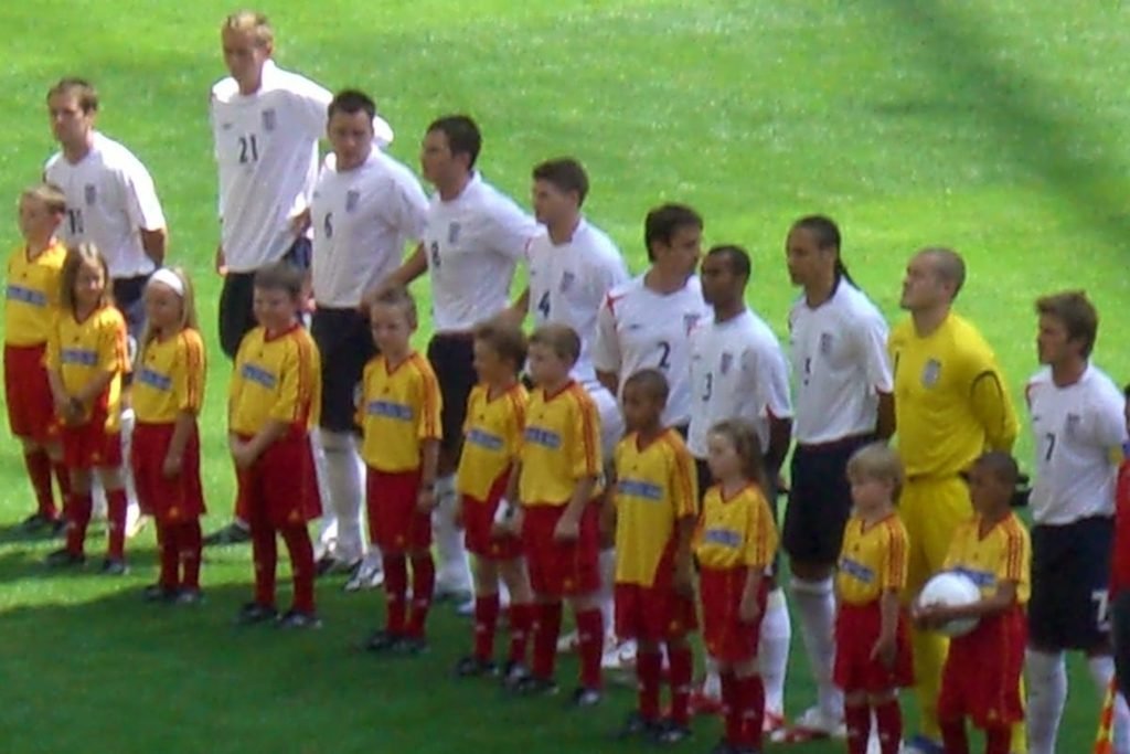 The England team in white standing in a line with mascots before a 2006 World Cup match.
