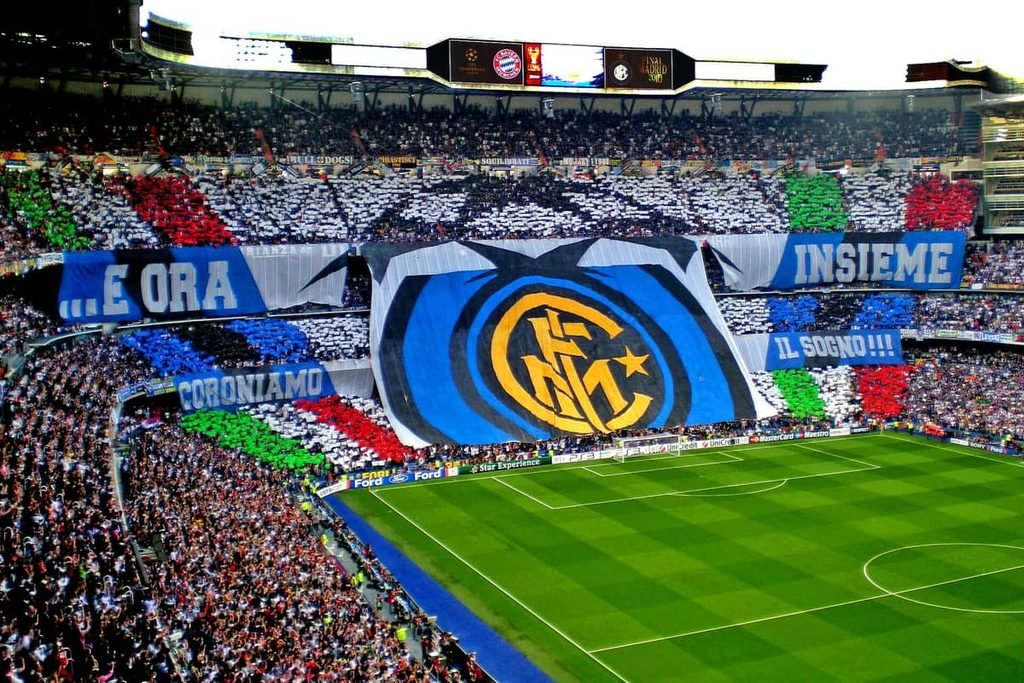 A stand full of Inter supporters holding up a giant blue and black Inter crest and banners inside the Bernabéu.