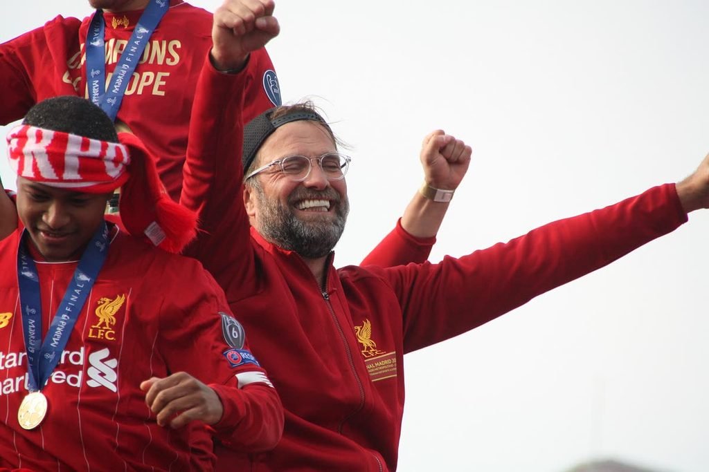 Jürgen Klopp laughing and raising his fist on an open-top bus.