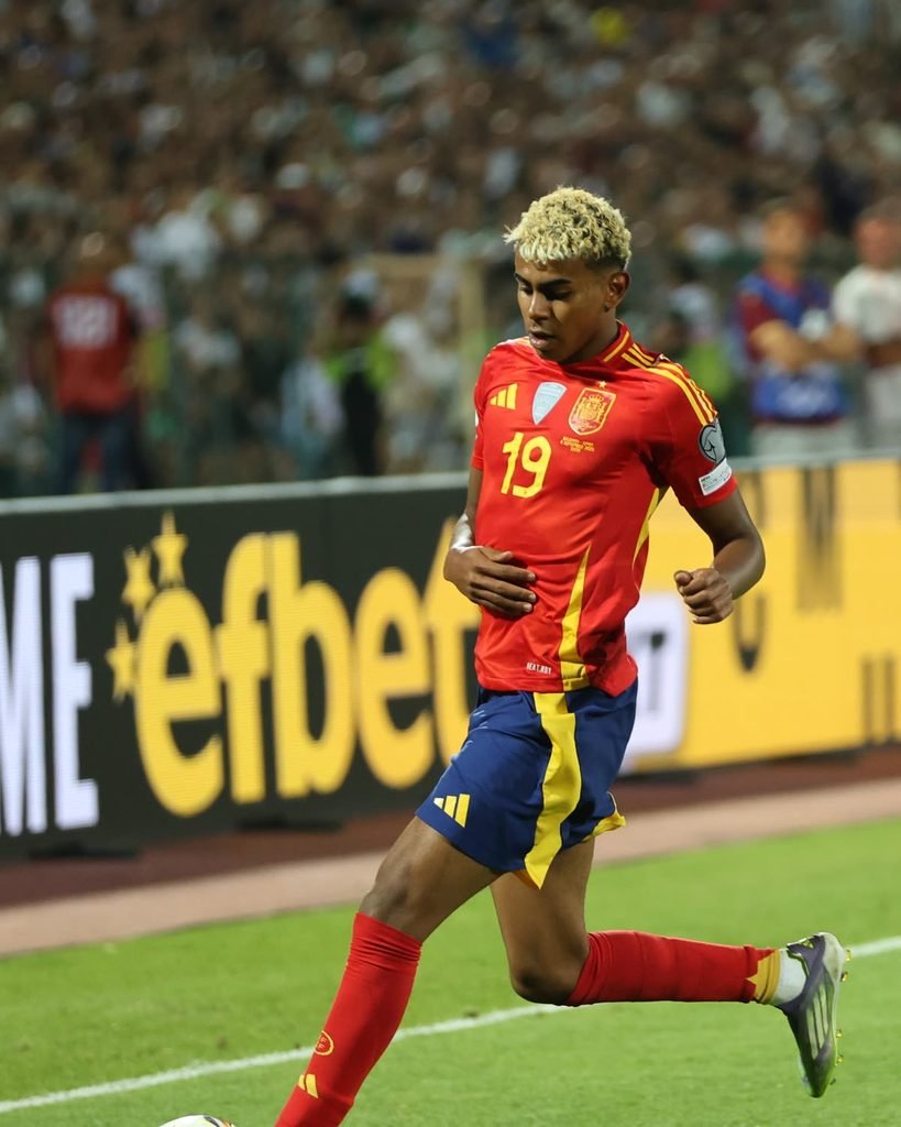 Lamine Yamal in Spain's red shirt and blue shorts, number 19, dribbling the ball.