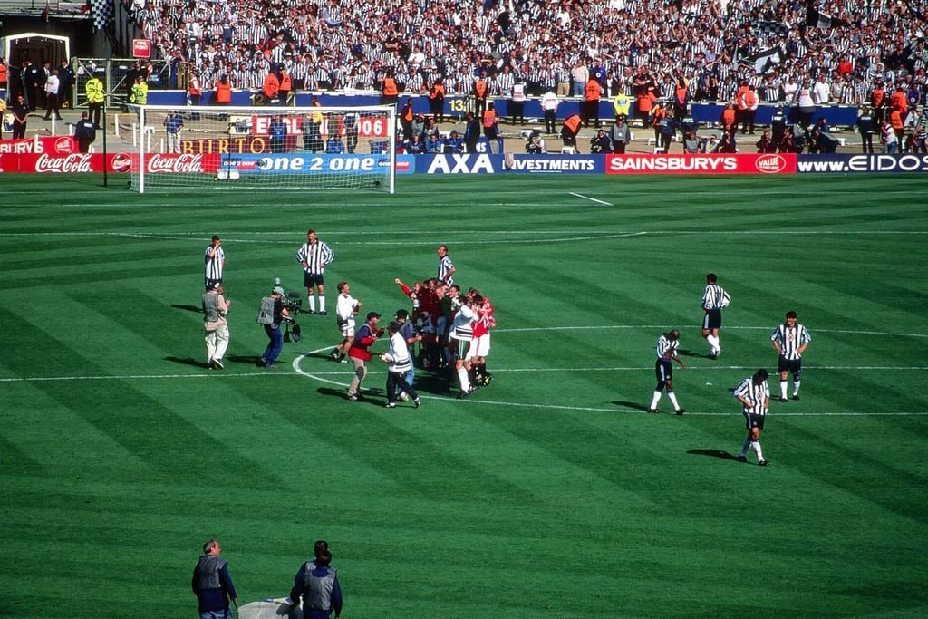 Manchester United players celebrating in a huddle on the Wembley pitch after the 1999 FA Cup final.