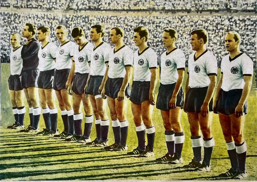 A colour magazine photo of eleven West Germany players in white shirts and black shorts standing in a line.